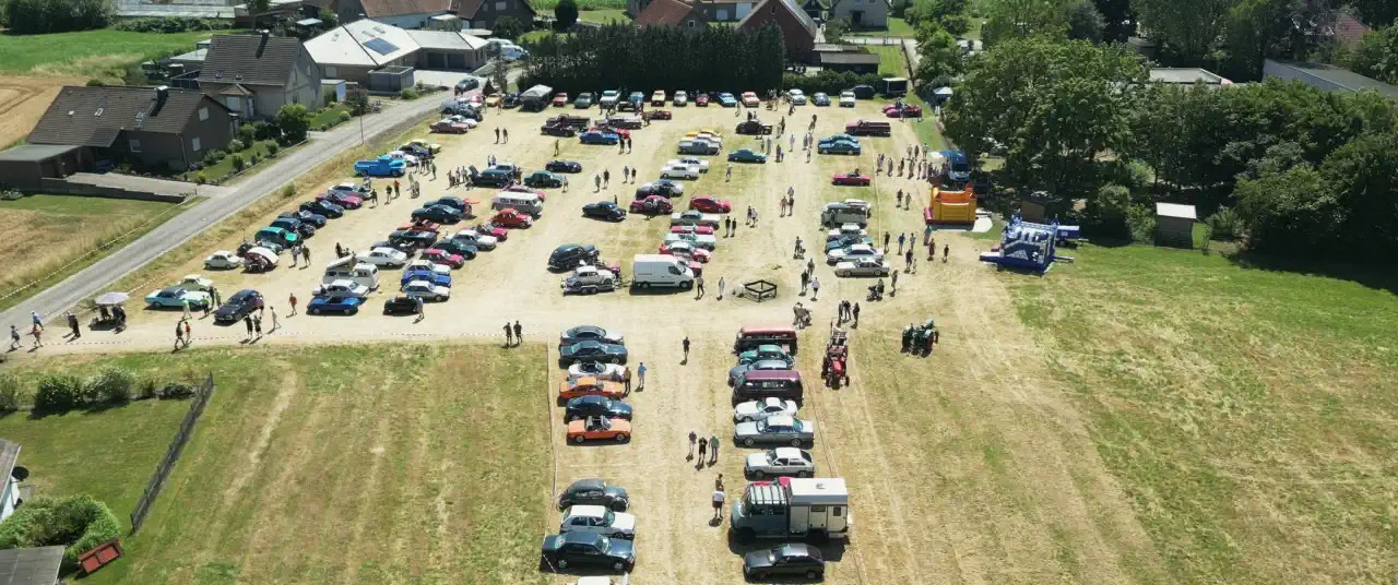 Luftaufnahme vom Oldtimertreffen in Ahle: Reihen von Oldtimern auf einer Wiese, dahinter Höfe, Bäume und Felder